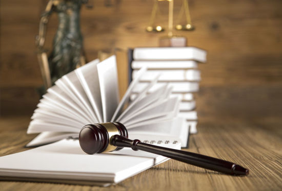 table with open book, gavel, stack of books and lady of justice statue